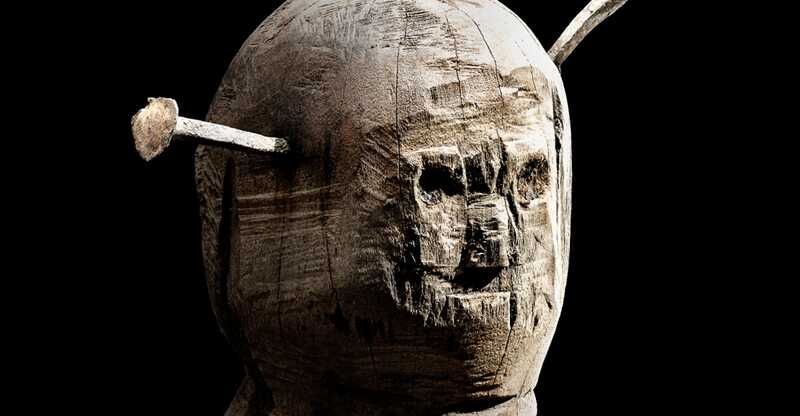 Darstellung einer sogenannten Nagelpuppe, einer Holzfigur in Form eines Menschen mit angedeutetem Gesicht und Eisennägeln, die in den "Kopf" gehämmert wurden.