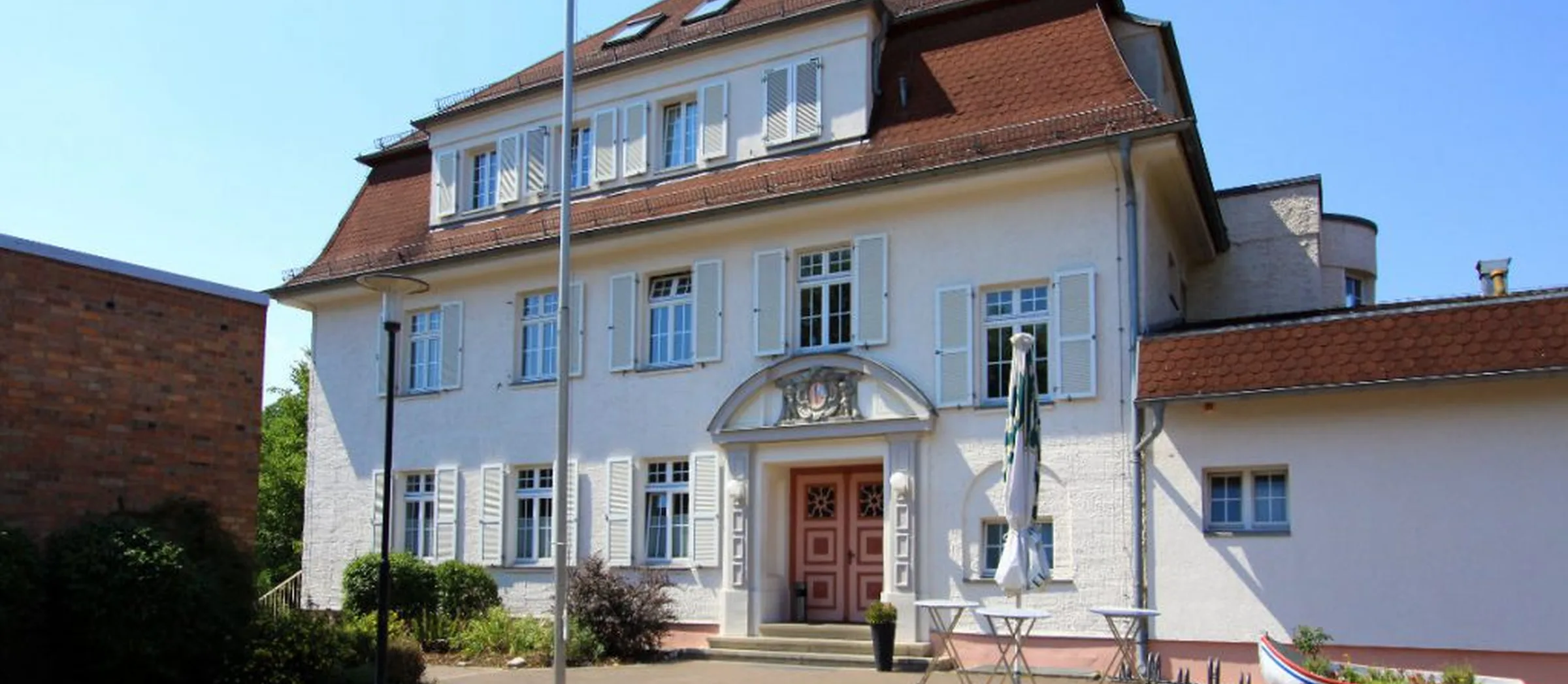 Ein weißes, schlossähnliches Gebäude wird umgeben von einem kleinen Vorgarten.