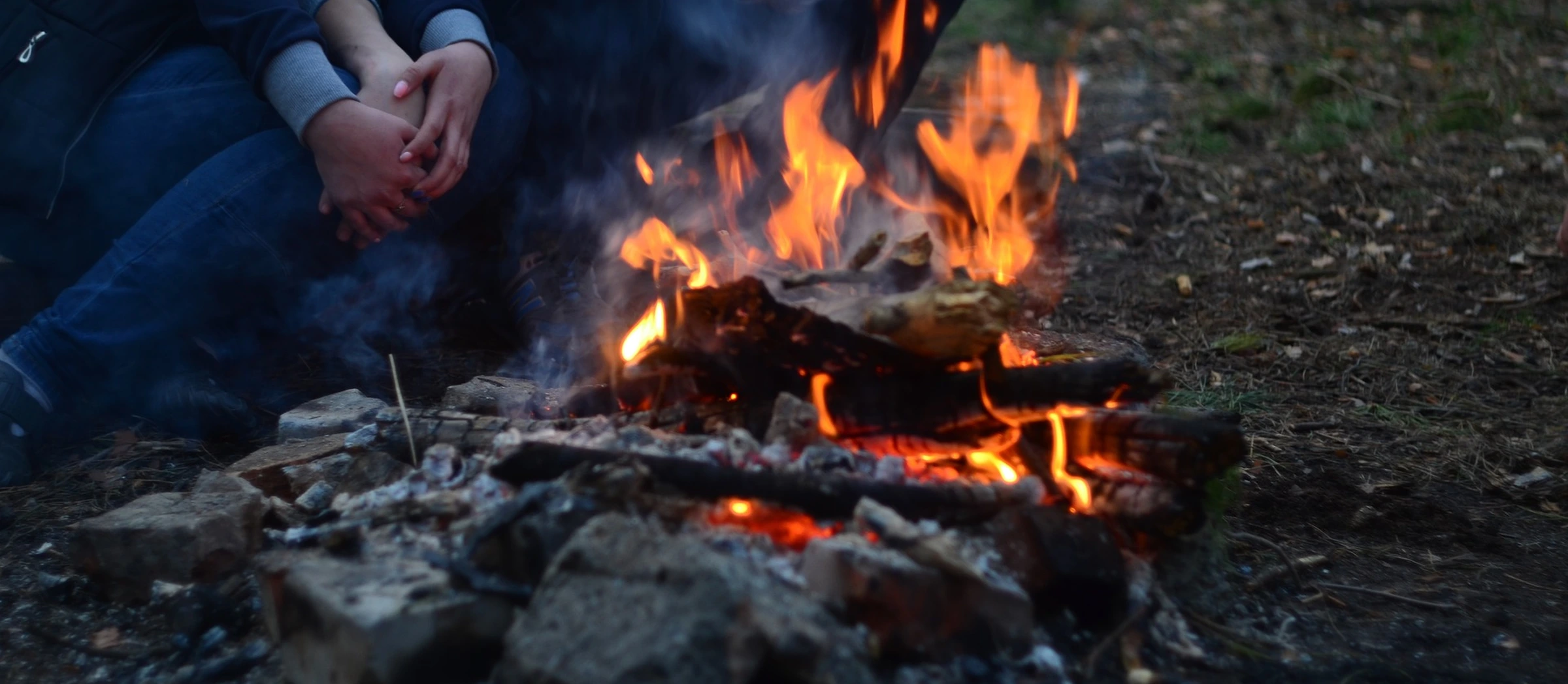 Ein Paar sitzt am Lagerfeuer, ihre Gesichter sind nicht zu sehen