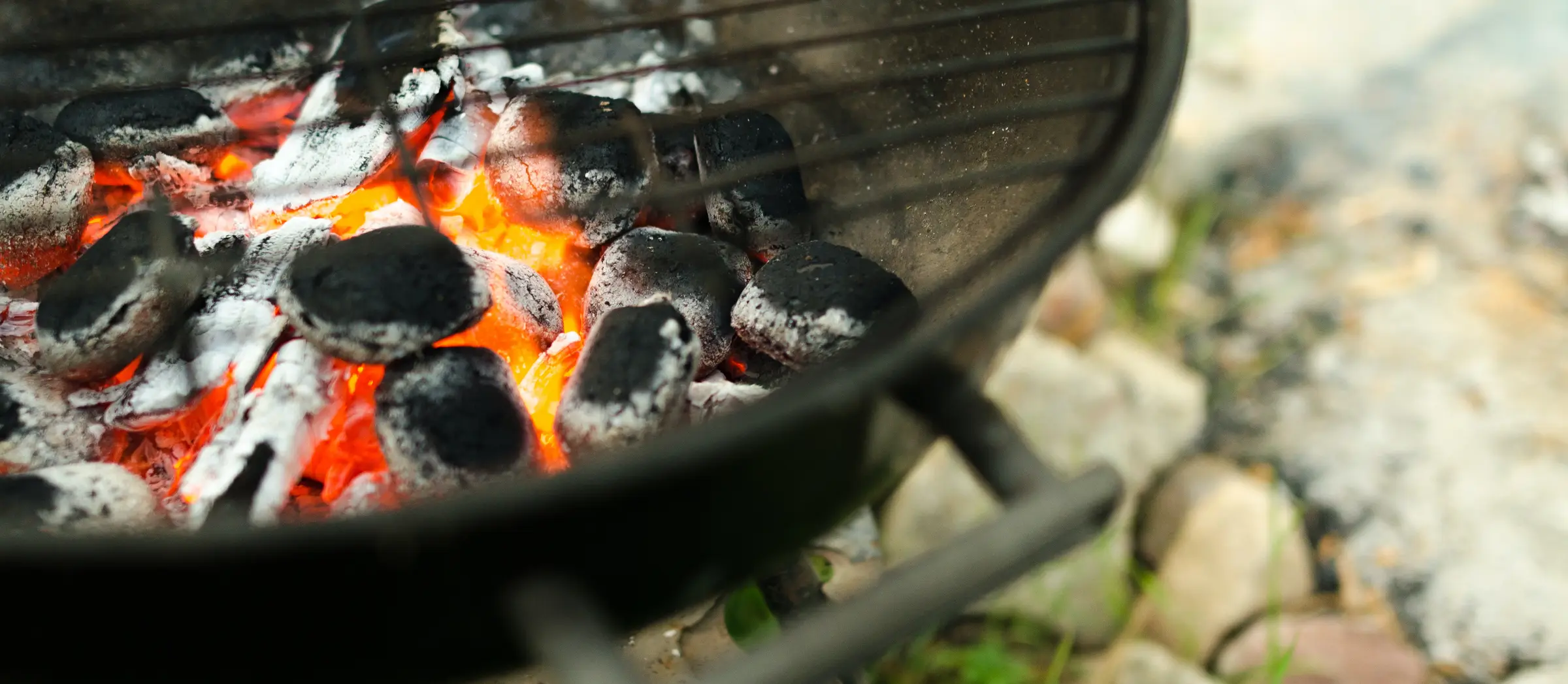 Unter dem Gitterrost eines Grills ist die flammende Glut zu sehen.