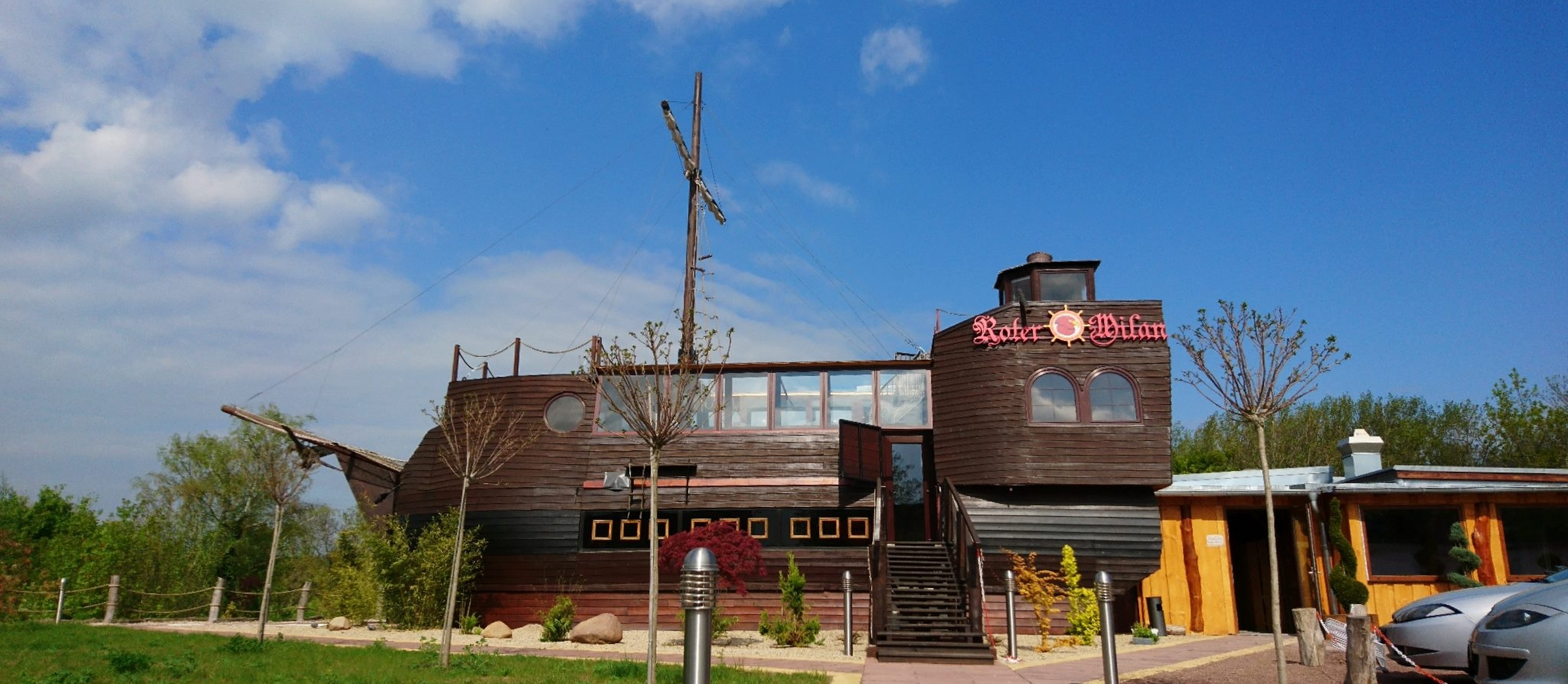 Blick auf eine Gaststätte, die von außen wie ein goßes Holzschiff aufgebaut ist. 