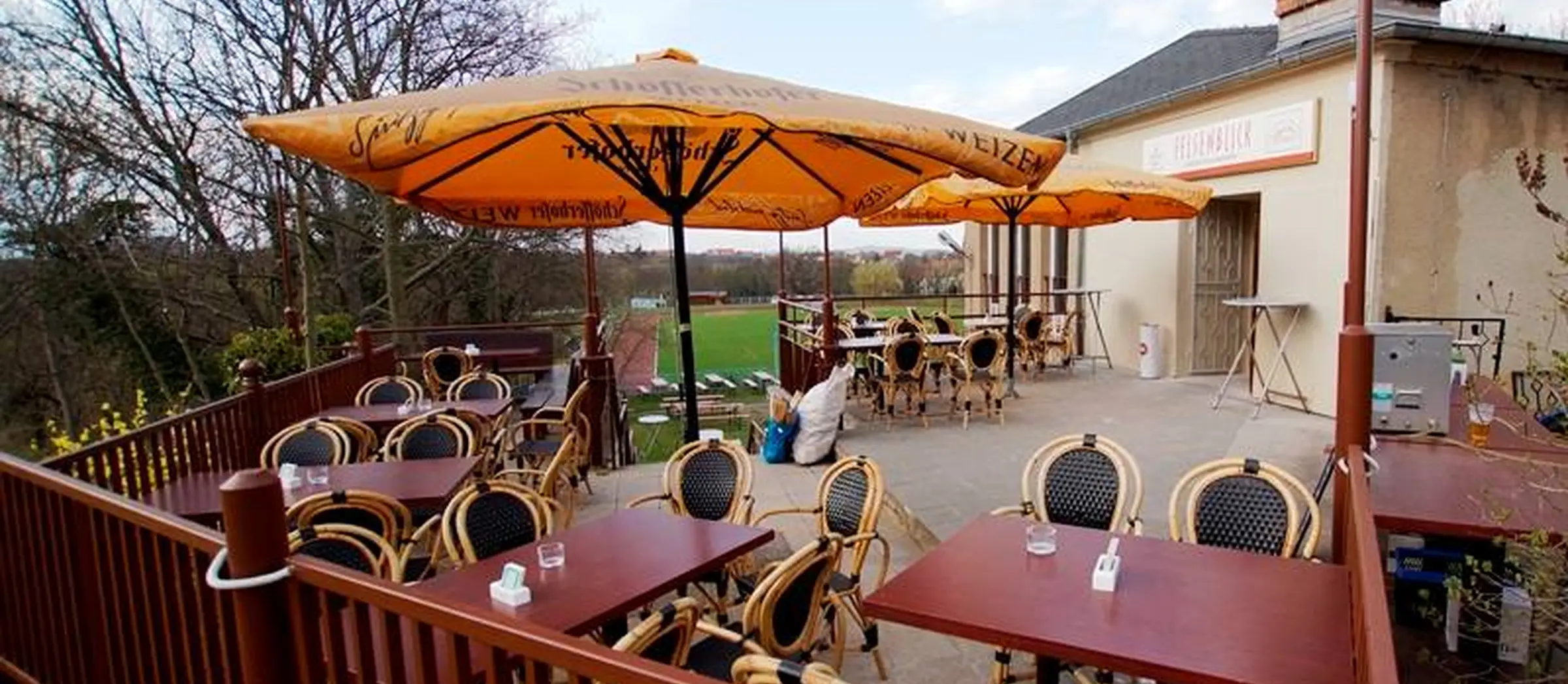 Auf der Terrasse der Gaststätte Felsenblick befinden sich gelbe Sonnenschirme und mehrere Tische und Stühle