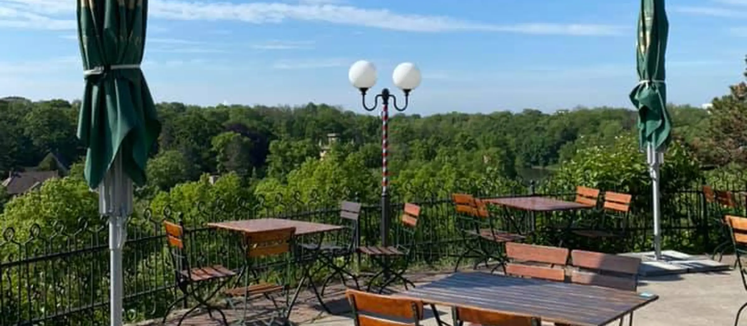 Auf einer Terrasse stehen vereinzelt Holzstühle und-tische mit Blick über das grüne Stadtbild.