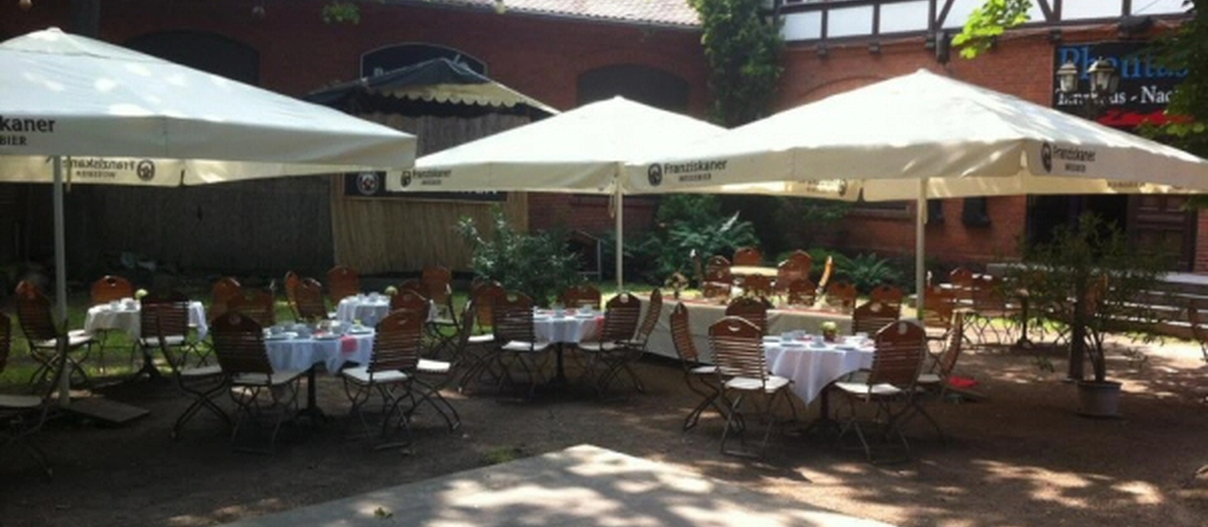 Blick auf den gemütlichen Biergarten des Waldkaters mit gedeckten Tischen und Sonnenschirmen