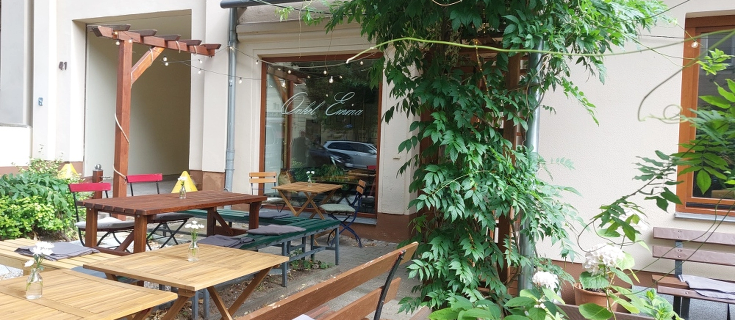 Das Bild zeigt den Außenbereich der Bar: Holzbänke und Pflanzen schmücken die Terrasse.