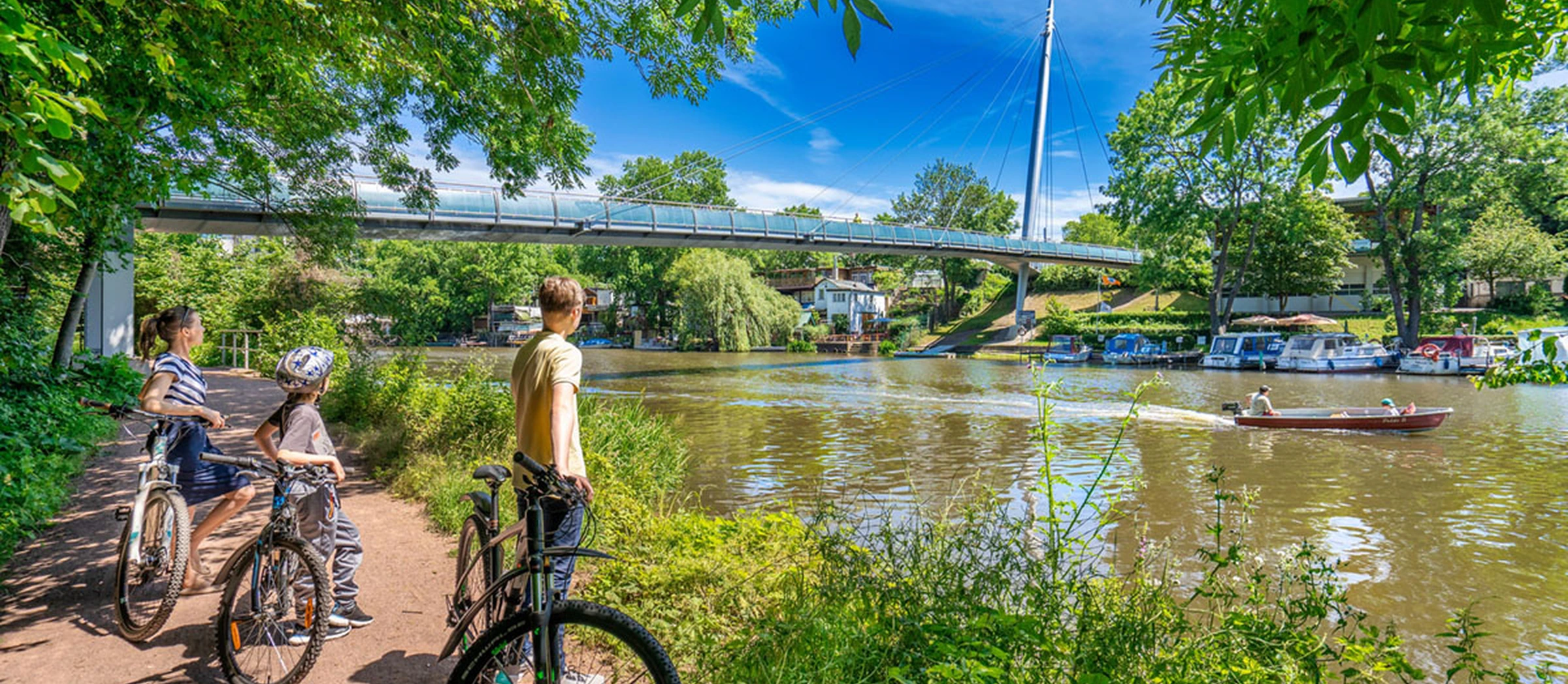 Fahrradfahrer*innen stehen am Ufer der Saale und blicken in Richtung Wasser