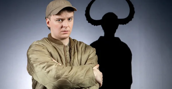 Franz Blumenstock sitzt in Gummistiefeln auf dem Boden. Er guckt verärgert. Im Hintergrund sind Schatten von einem Kind mit Hörnern.