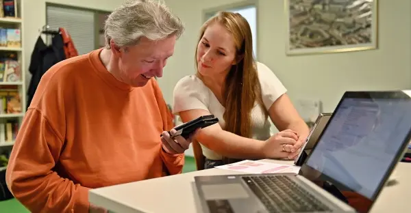 eine ältere Person lässt sich von einer jüngeren erklären wie ein Handy funktioniert