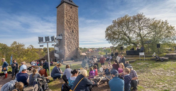 Eine Gruppe verschiedener Menschen sitzt im Gras vor einem Burgturm.