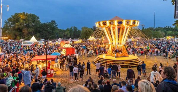 Ein bunt beleuchtetes Kettenkarusell inmitten eines Jahrmarktes.