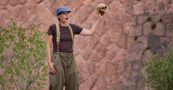 Eine Schauspielerin steht auf einer Open-Air-Bühne und spricht, während sie einen Totenschädel hochhält.