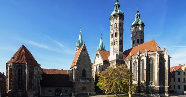 Der Naumburger Dome wird vom Sonnenlicht erstrahlt. Er hat 4 Kirchtürme und einen kleinen grünen Vorplatz.