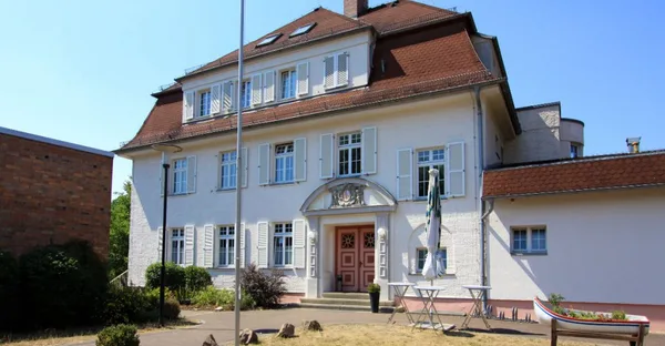 Ein weißes, schlossähnliches Gebäude wird umgeben von einem kleinen Vorgarten.