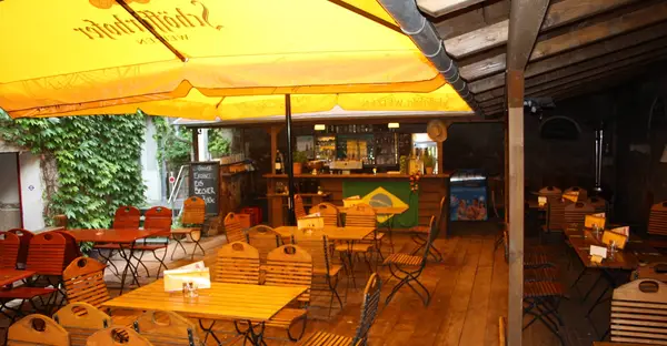 Blick auf die Terrasse des Café Deix mit gelben Sonnenschirmen und Holztischen. Im Hintergrund sieht man eine kleine Bar.