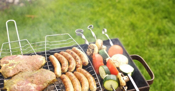Würste, Steaks und Gemüsespieße liegen auf einem Grillrost