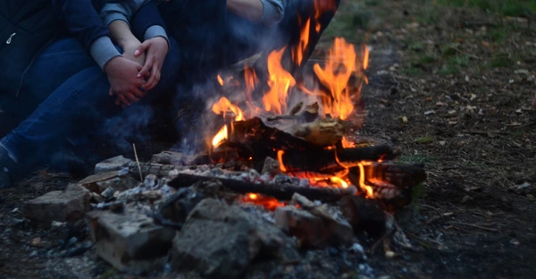 Ein Paar sitzt am Lagerfeuer, ihre Gesichter sind nicht zu sehen