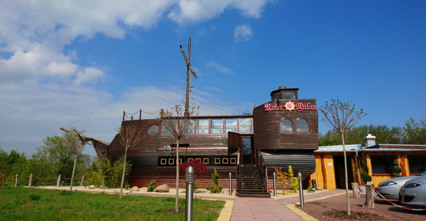 Blick auf eine Gaststätte, die von außen wie ein goßes Holzschiff aufgebaut ist. 