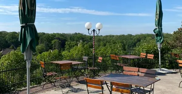 Auf einer Terrasse stehen vereinzelt Holzstühle und-tische mit Blick über das grüne Stadtbild.