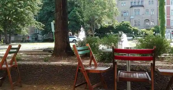 Blick auf den August-Bebel-Platz: Holzstühle und Bäume umgeben den Springbrunnen am August-Bebel-Platz.