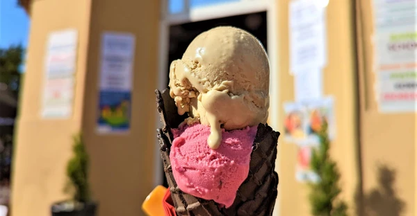 Auf dem Bild sieht man ein Eis mit 2 Eiskugeln (in pink und hellbraun) und einer schwarzen Waffel.