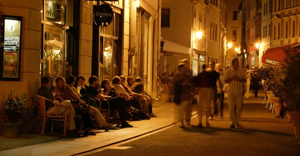 Nächtliches Treiben in der Kleinen Ulrichstraße: Menschen sitzen draußen oder flanieren durch die Fußgängerzone.