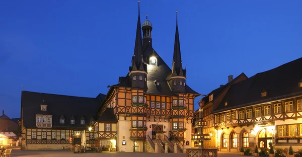 Ein Gebäude im Fachwerkhaus-Stil mit 2 Türmen wird in der Abenddämmerung von strahlenden Lichtern beleuchtet.