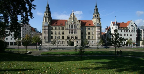 Blick auf den Hansering: Im Vordergrund ist eine Wiese zu sehen, im Hintergrund ein schlossartiges Gebäude mit 2 Türmen.