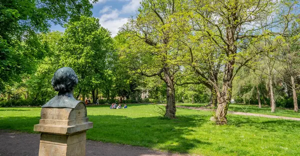 Im Vordergrund ist eine Statue zu sehen, im Hintergrund eine gepflegte grüne Parkanlage. 