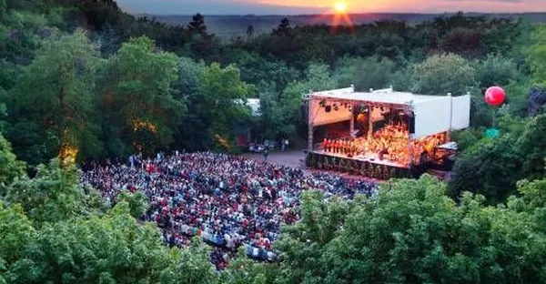 Konzert in der Galgenbergschlucht: Viele Menschen lauschen einem Konzert auf einer Open Air Bühne bei Sonnenuntergang.