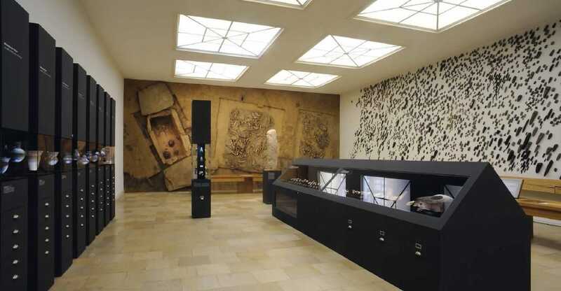 Blick in den Raum der Dauerausstellung zeigt das senkrecht an die Wand montierte Steinkistengrab des Rinderbarons von Westerhausen, mehrere Vitrinen mit archäologischen Funden sowie die lange Wand des Ausstellungssaals, die vollkommen bedeckt ist mit Steinbeilen.
