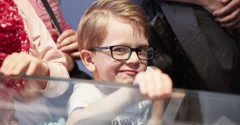 Ein Kind blickt über eine Museumsvitrine in die Kamera und lächelt