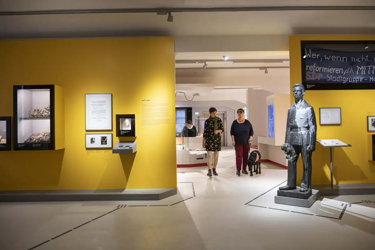 Ein sehbeeinträchtigte Frau mit Assistenzhund wird durch die Dauerausstellung des Stadtmuseums geführt.