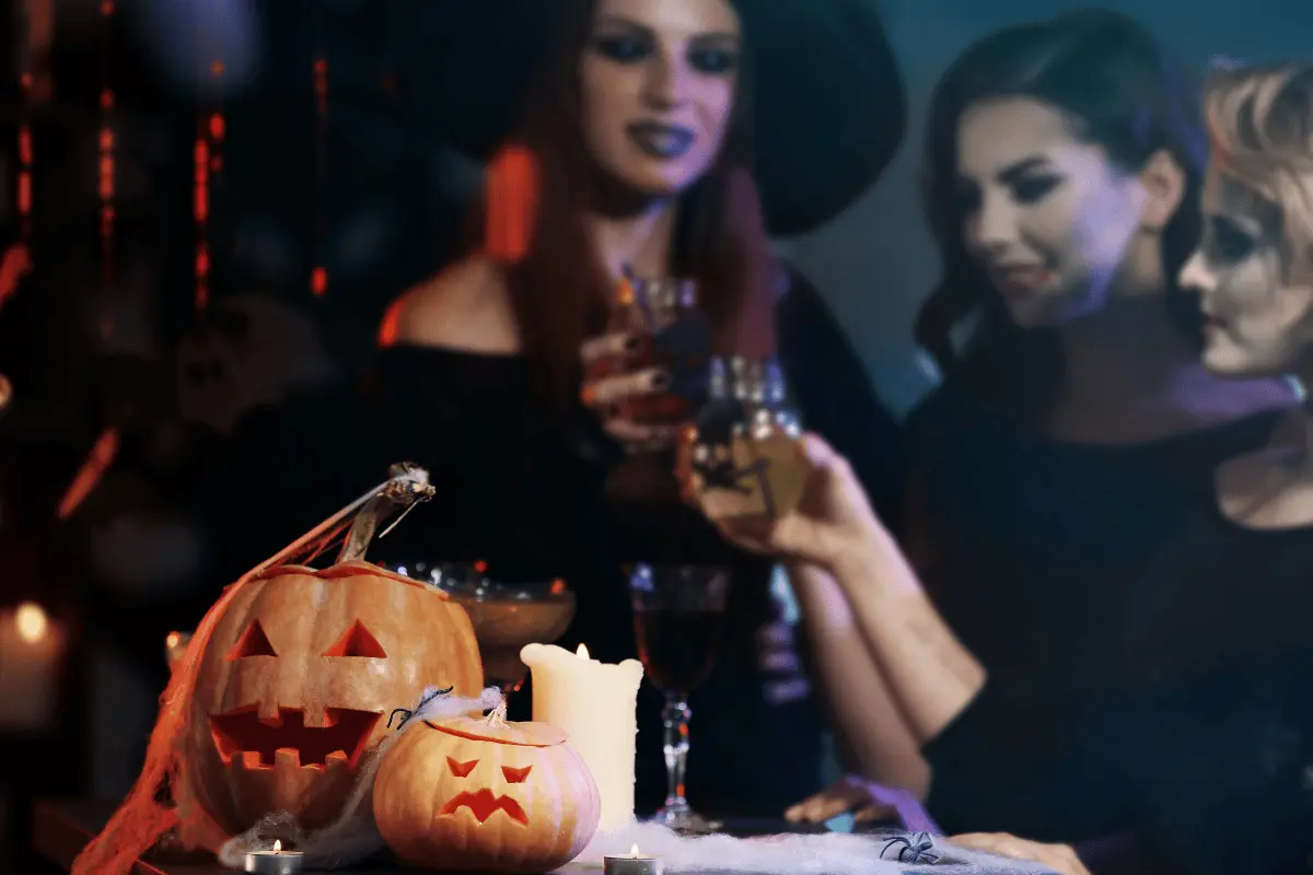 Im Vordergrund ein geschnitzter Kürbis, im Hintergrund feierende, kostümierte Personen