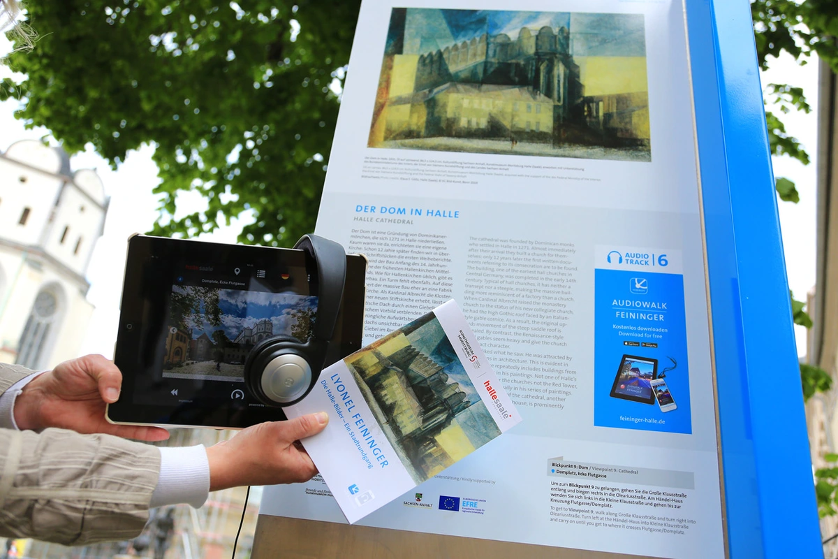 Crossmedialer Audiowalk mit einer Texttafel, einem Tablet, Kopfhörern und einer Broschüre